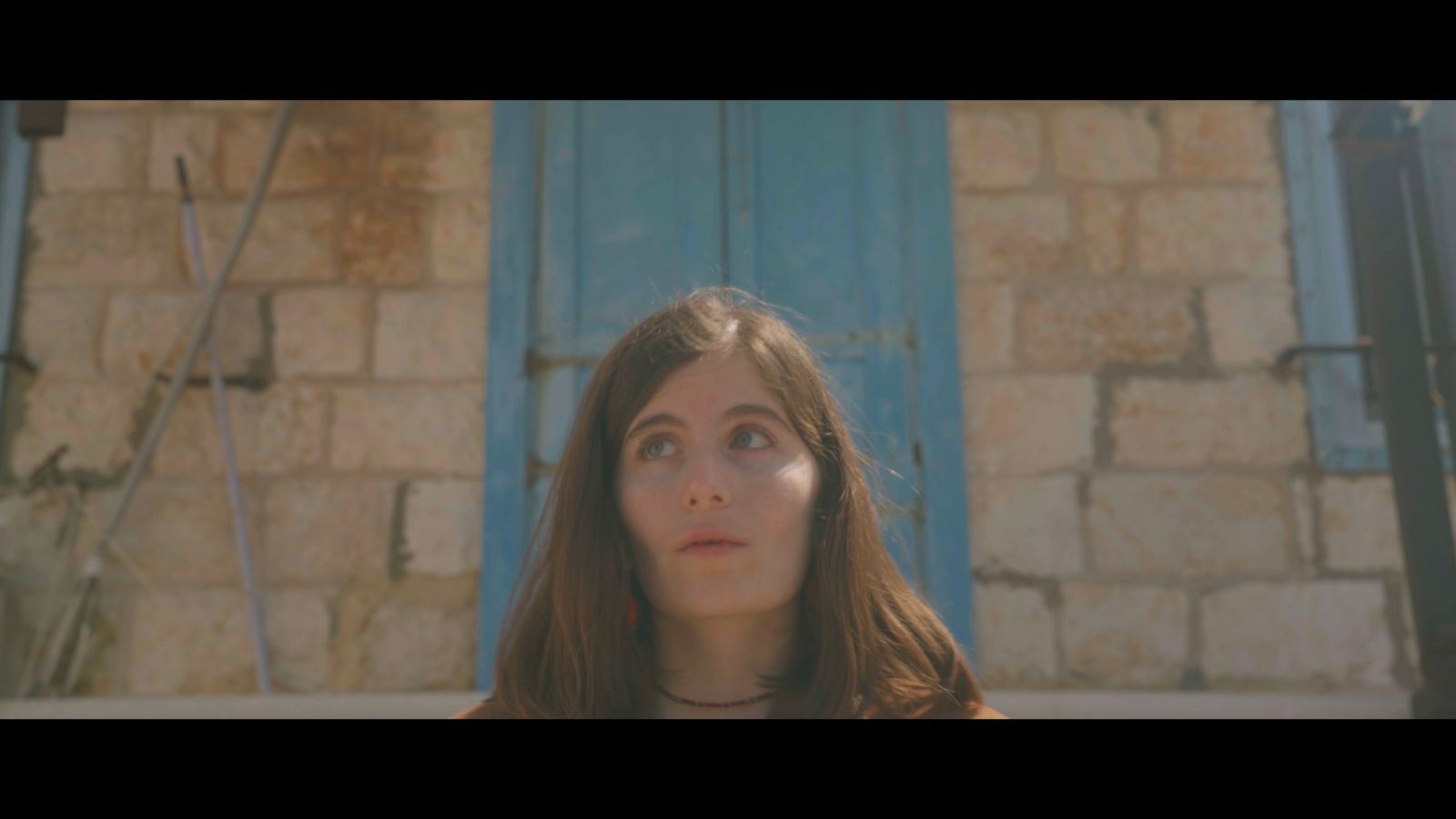 Film still of a woman framed against stone and blue shutters